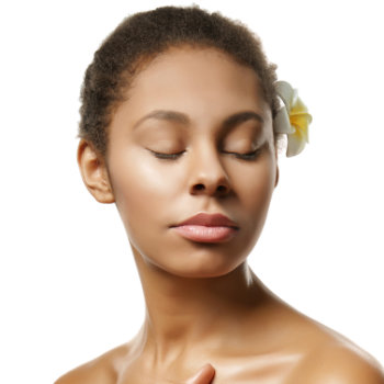A woman with short hair and a flower tucked behind her ear closes her eyes and faces slightly left against a white background.