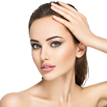 Close-up of a person with green eyes, light makeup, and a hand resting on their head, against a plain white background.