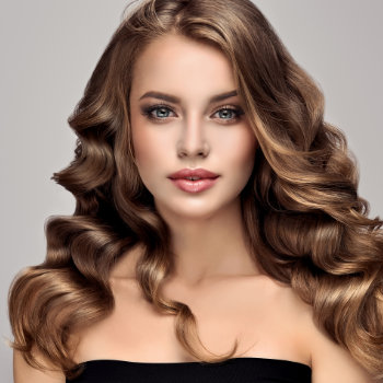 A woman with long, wavy, brunette hair and light makeup is wearing a black strapless top. She poses in front of a neutral background.