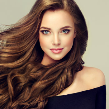A woman with long, flowing brown hair and blue eyes is wearing an off-the-shoulder black top. She is smiling slightly against a neutral background.