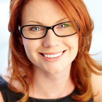 A woman with red hair and glasses smiles, wearing a black top.