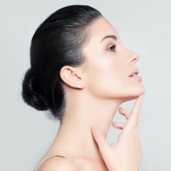 Profile view of a person with dark hair styled in a low bun, touching their chin with one hand against a plain, light-colored background.